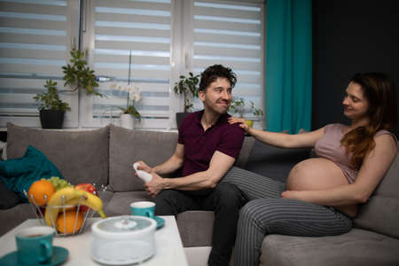 A husband massages his wifes feet and they sit together on the sofa in the living room. Pregnant woman.の写真素材