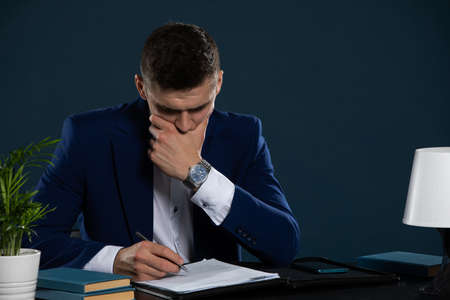 A young businessman is thinking hard about signing a new loan agreement.の写真素材