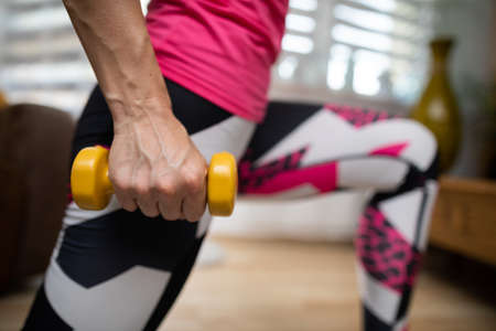 A woman squeezes a dumbbell tightly in her hand during her morning exercise at home.
