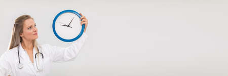 The doctor holds a wall clock in her hands and reminds us that its time to treat. Panoramic frame.の写真素材