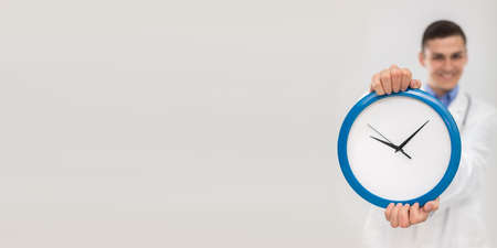 The doctor holds a wall clock in his hands measuring the daily time. Panoramic view.の写真素材