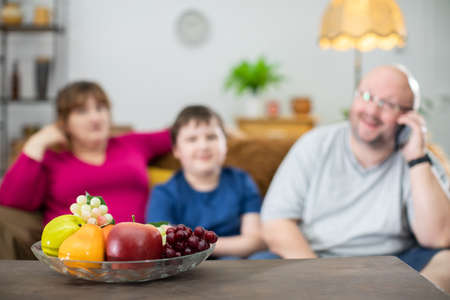 The brown table and its delicious fruit stand and on the sofa sits a family ready to lose weight.