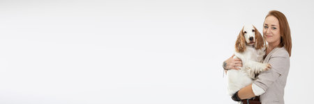 A woman holds a dog in her arms and they both look into the camera. Panoramic frame. English cocker spaniel with honey gold coat.の写真素材