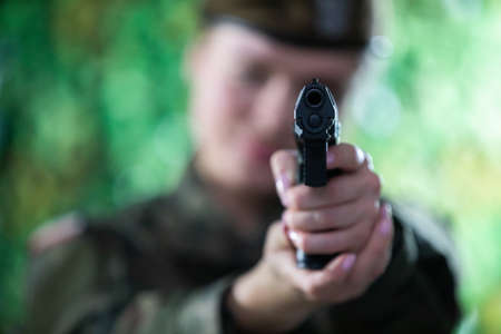 The lady soldier aims straight at the camera with a short gun.の写真素材