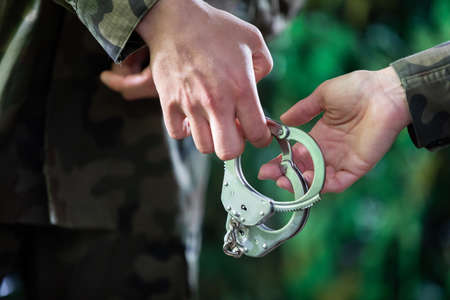 Soldiers pass metal handcuffs from hand to hand. Close-up view.
