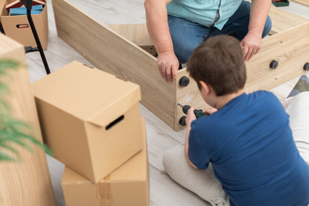 Dad showed his son how to assemble the bookcase, now he screws the screws himself with a screwdriver. Working together while assembling furniture.の写真素材