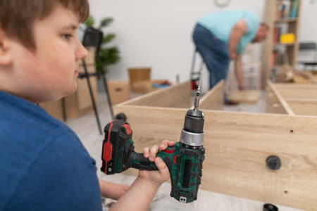 A young boy holds a cordless screwdriver in his hand and wonders.の写真素材