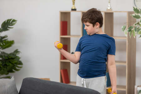 A young boy trains with dumbbells for health.の写真素材