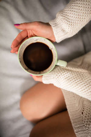 Neat female legs on sofa. Close-up view of a cup of coffee while relaxing.の写真素材