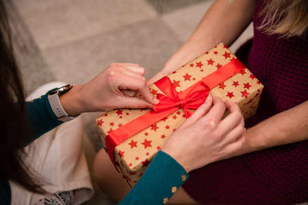 Daughter ties a bow on a gift package and mom holds the package.の写真素材