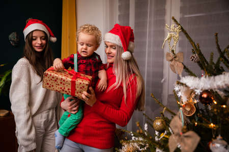 A mom and big sister give a gift to a two-year-old child at Christmas.の写真素材