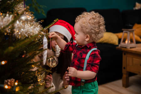 The little boy hangs the ornaments on the Christmas tree and the older sister watches.の写真素材