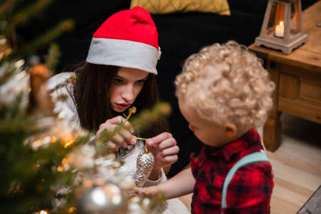 A sister helps her young brother hang ornaments for the Christmas tree.