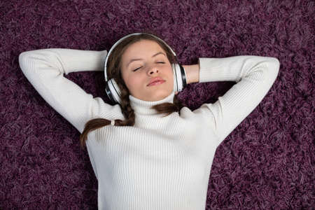 A teenager lies on the carpet and listens to music on wireless headphones.の写真素材