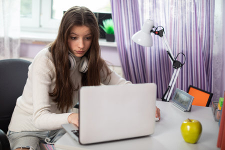 A young girl ogles and listens to a school lecture at home on a laptop.の写真素材