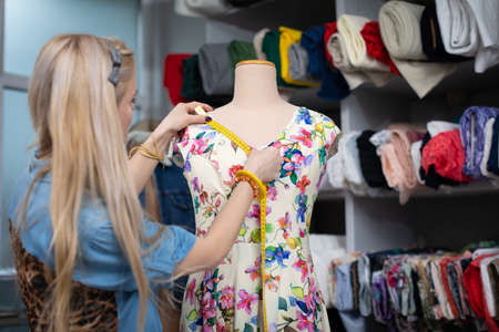 A seamstress measures a dress hanging on a mannequin with a tailors centimeter.の写真素材