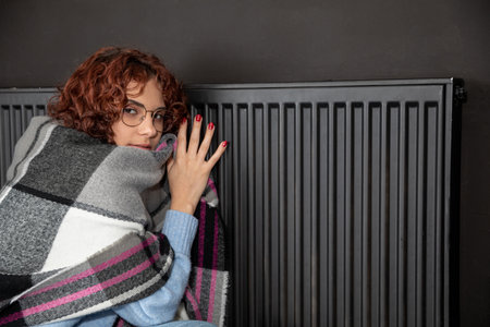 A girl huddled around a hot radiator. The first start of the central heating system.