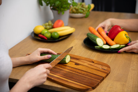A woman slices a cucumber for a salad on a wooden board.の写真素材