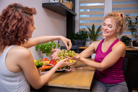 women sitting in the kitchen serving themselves grapes over the tableの写真素材