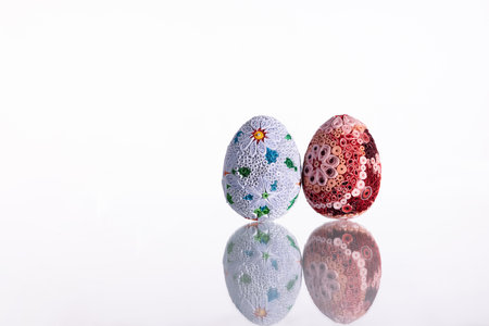 Two Easter eggs on a white background reflected in a glassy ground.の写真素材