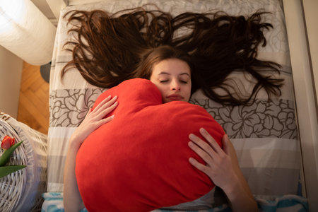 A red pillow in the hands of a sleeping girl.の写真素材