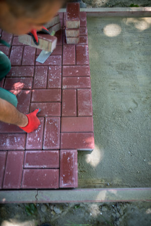 A conscientious blue-collar worker lays red paving stones in a designated area.の写真素材