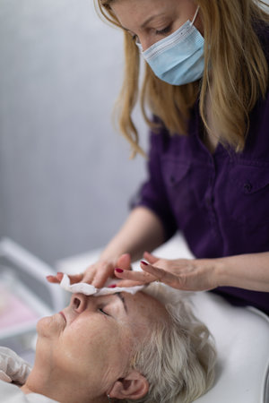 An experienced beautician prepares the patients forehead skin for further treatments.の写真素材