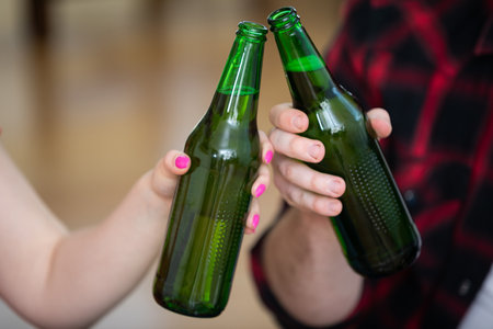 Large close-up on two beer bottles held by a boy and a girl.