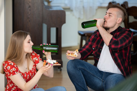 A girl and her boyfriend on a date sit at home, eat pizza and drink beer.