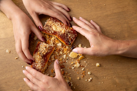 Hands Reaching for a Delicious Pastry on a Rustic Wooden Table Filled with Treatsの写真素材