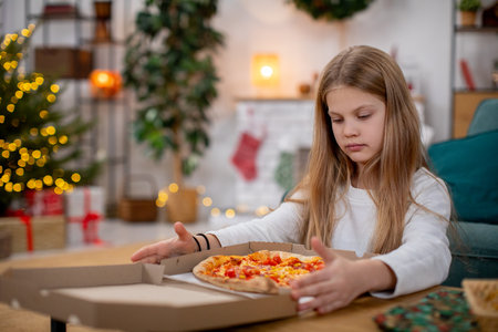 A Girl Enjoying a Slice of Pizza in a Cozy and Inviting Holiday Setting Filled with Joyの写真素材