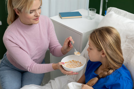 A Caring Mother Gently Feeds Her Sick Child Who is Resting in Bed to Provide Comfort