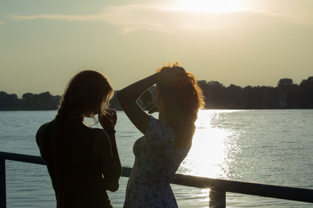 Silhouettes casting shadows at Sunset by the tranquil Water as friends gather togetherの写真素材