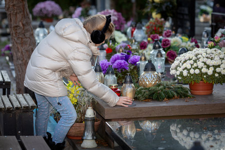 A person places a glowing candle among vibrant flowers in a serene cemeteryの写真素材