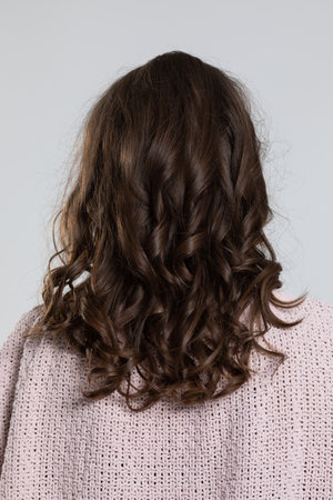 A woman depicted from the back, showcasing her curly brown hair under soft and gentle lightingの写真素材