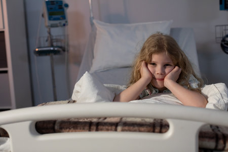 A young child in a hospital bed looks reflective and deep in thought about their situationの写真素材