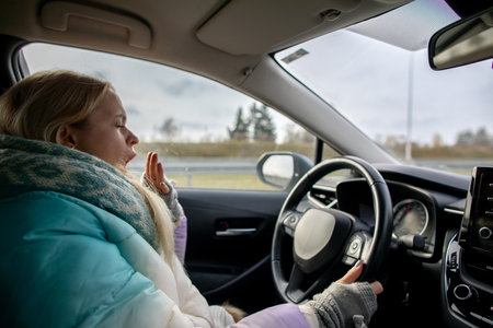 A driver is yawning while sitting in the cozy interior of a car during a chilly winter dayの写真素材