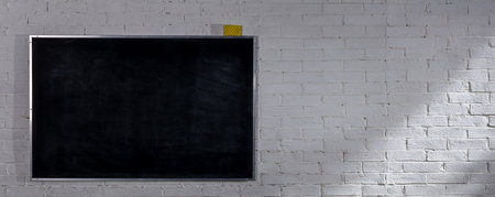 A minimalistic black chalkboard beautifully displayed on a classic white brick wall backgroundの写真素材