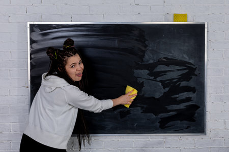 A young woman is diligently engaged in the task of cleaning a chalkboard using a sponge toolの写真素材