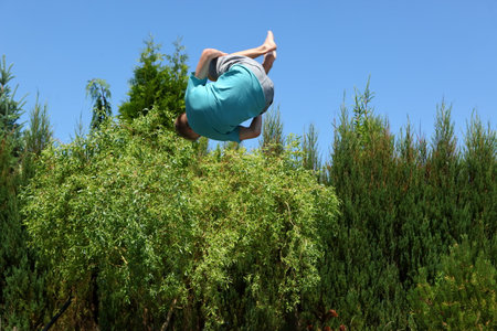 A Dynamic Backflip Displayed Against a Beautiful Blue Sky and Lush Greenery in Natureの写真素材