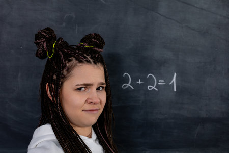 A confused student stands before an incorrect math equation on the chalkboard, puzzledの写真素材