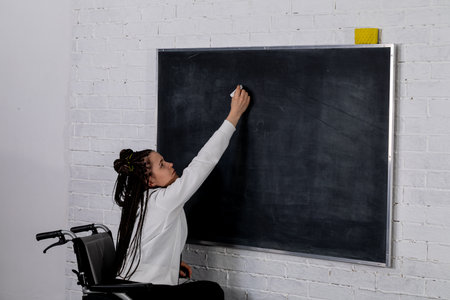 A woman writes on a black chalkboard in a modern classroom, highlighting creativity and educationの写真素材