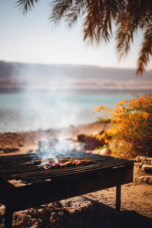Enjoy a serene lakeside barbecue while smoke gently drifts over the peaceful water nearbyの素材