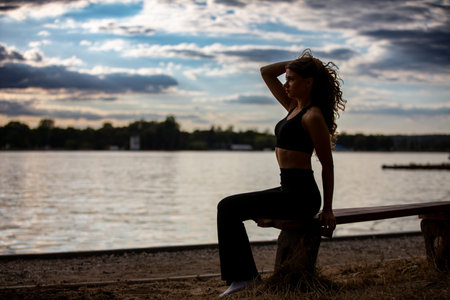A Woman Relaxing Outdoors by the Peaceful Water During Dusk, Surrounded by Natures Beautyの写真素材