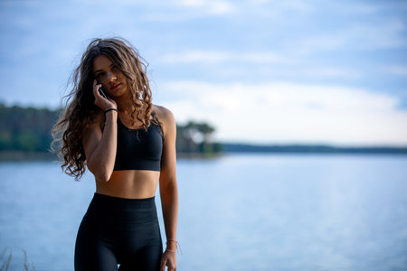 A Young Woman with Curly Hair Enjoying the Serenity of Water at Dusk by the Shoreの写真素材