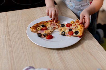 A Joyful Child Happily Enjoying Delicious Pizza on a Beautifully Set Wooden Tableの写真素材