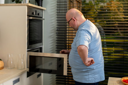 A man is cooking in a modern kitchen that includes an oven and various necessary toolsの写真素材