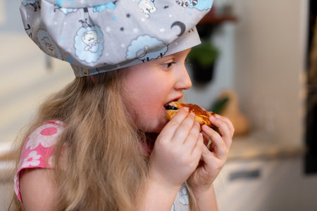 A Young Chef, Dressed in a Colorful and Fun Hat, is Happily Enjoying a Delicious Slice of Pizzaの写真素材