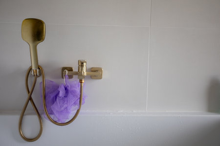 Luxury fixtures on tiled wall, Relaxing bathing area featuring gold and purple accents, Serene bathroom ambiance highlighted by elegant fixtures and textured grout detailsの写真素材