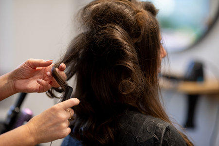 Rear view stylist teasing hair volume, hands backlighting frizz and texture visible, fingers shaping...
